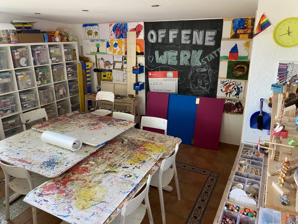 Ein Blick in unsere Offene Werkstatt mit großem Basteltisch in der Mitte und vielen Materialien-Boxen drum herum