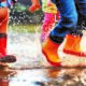 Blick auf Kinderfüße in Gummistiefeln, die in Pfützen springen