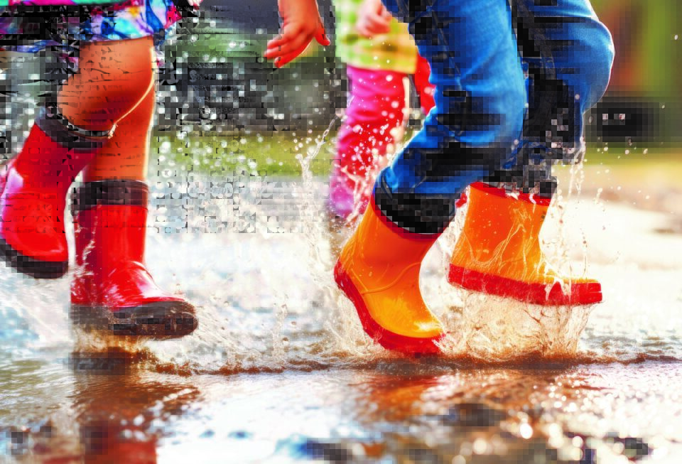 Blick auf Kinderfüße in Gummistiefeln, die in Pfützen springen